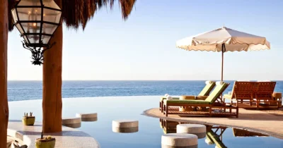 Luxury oceanfront pool area with lounge chairs, sun umbrellas, and a still infinity pool overlooking the calm blue sea in Los Cabos.