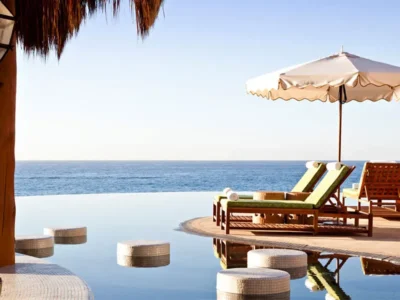 Luxury oceanfront pool area with lounge chairs, sun umbrellas, and a still infinity pool overlooking the calm blue sea in Los Cabos.