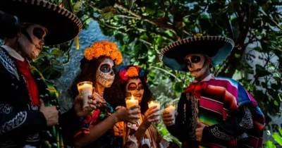 Day of the Dead celebration in Los Cabos with people wearing traditional skull makeup, colorful costumes, and holding candles during a nighttime gathering.