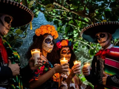Day of the Dead celebration in Los Cabos with people wearing traditional skull makeup, colorful costumes, and holding candles during a nighttime gathering.