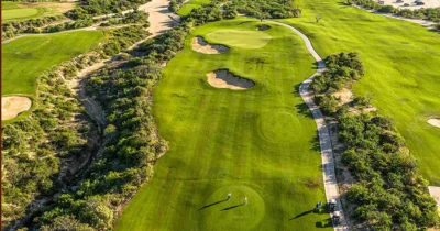 Aerial view of a lush golf course in Los Cabos with rolling fairways, sand bunkers, and surrounding desert vegetation.