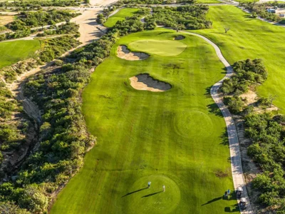Aerial view of a lush golf course in Los Cabos with rolling fairways, sand bunkers, and surrounding desert vegetation.