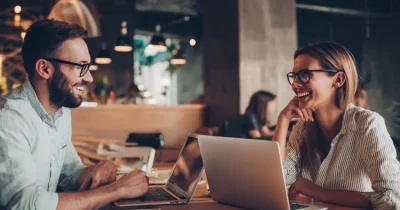 Two professionals working on laptops at a cafe in Los Cabos, with a relaxed indoor setting and a comfortable environment for remote work.