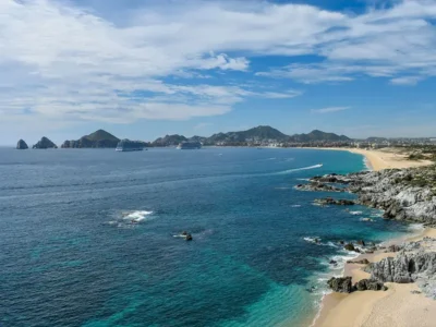Aerial view of the Los Cabos coastline with turquoise waters, sandy beaches, and the city skyline stretching along the shore in Baja California Sur.